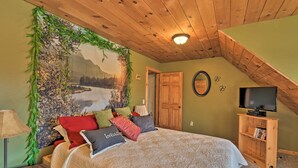 A bedroom with a bed, pillows, a TV stand, and a painting of a mountain landscape.