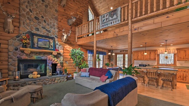 A log cabin interior with a stone fireplace, a sofa, a dining area, and a kitchen.