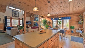 A spacious log cabin interior with a large kitchen island, wooden ceiling, and rustic decor.