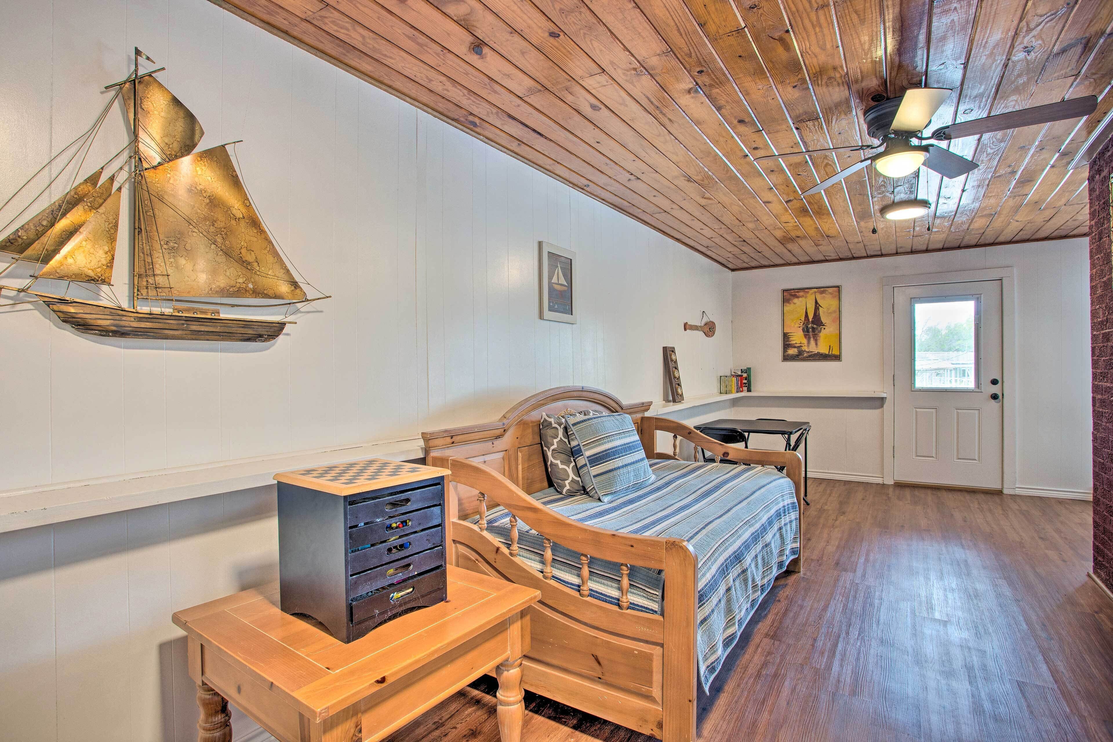 A bedroom with a wooden bed, a desk with drawers, a ceiling fan, and a sailboat decoration on the wall.