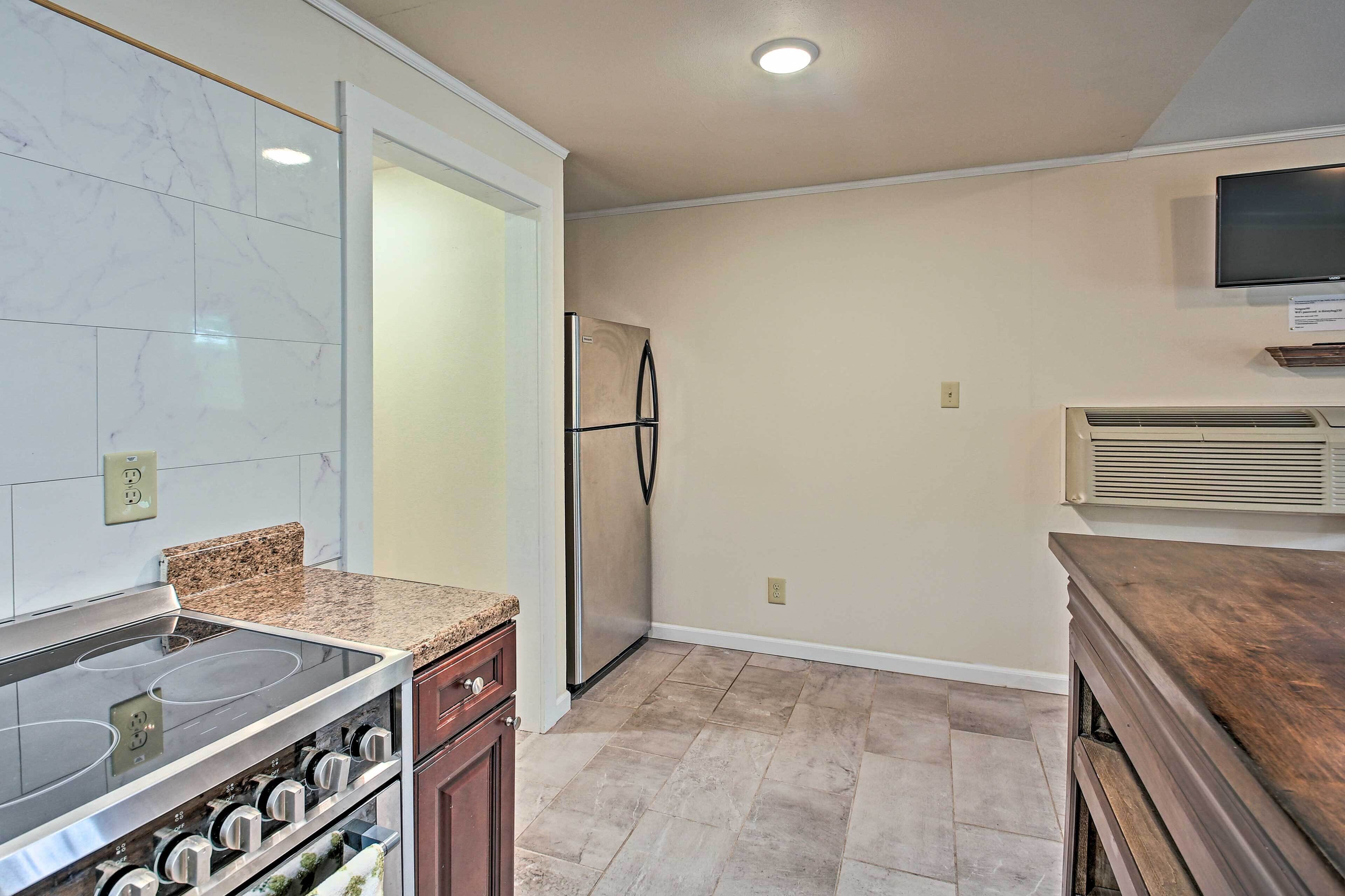 A kitchen with a built-in stove, oven, granite countertop, stainless steel refrigerator, and a wall-mounted TV.
