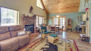 A spacious living room with a fireplace, a wooden ceiling, and a large window. - 9 Mi to Rainbow Lake: Woodsy Pinetop Cabin w/ Deck (Pinetop)