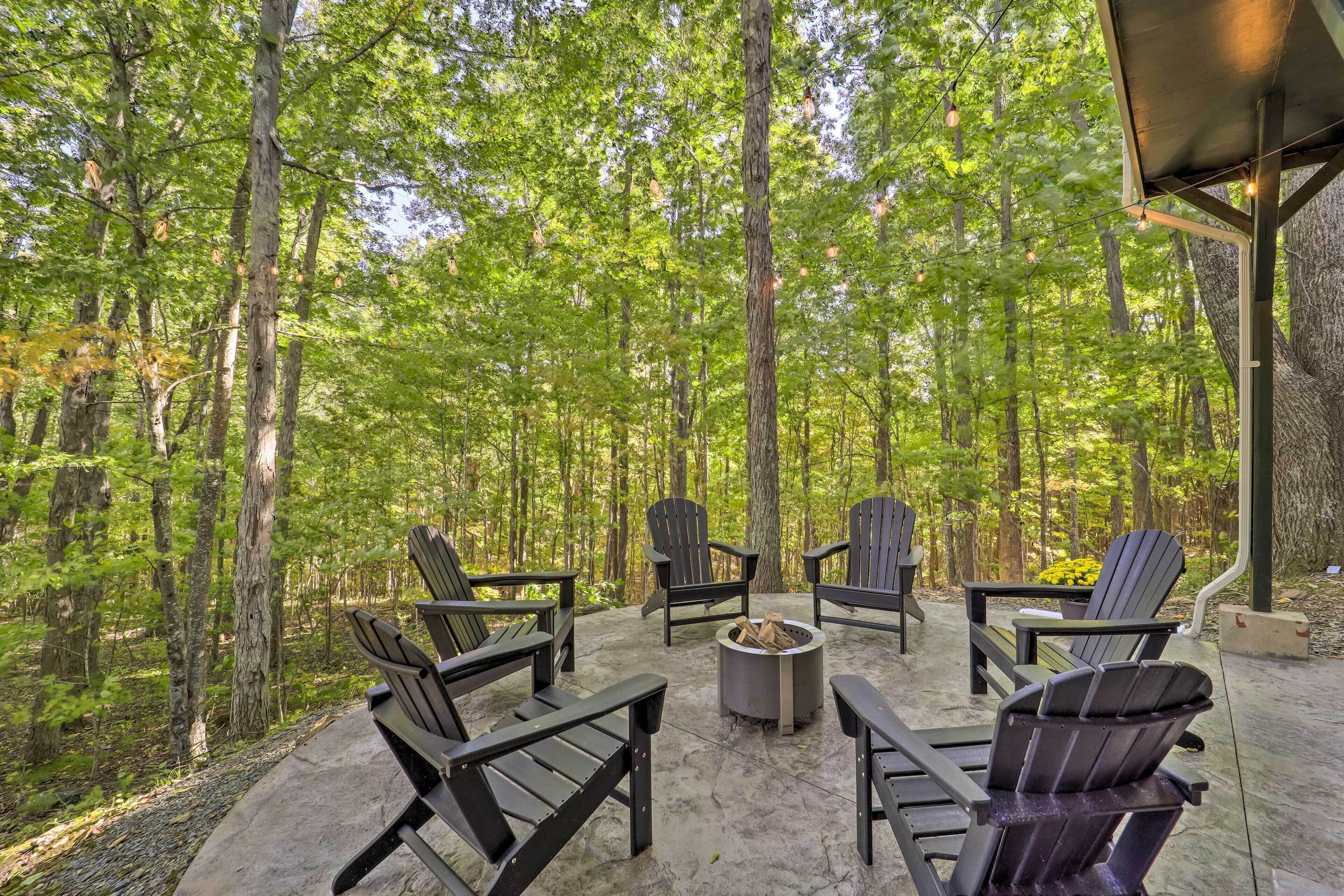 Un espacio de estar al aire libre con sillas Adirondack y una fogata rodeada de bosque.