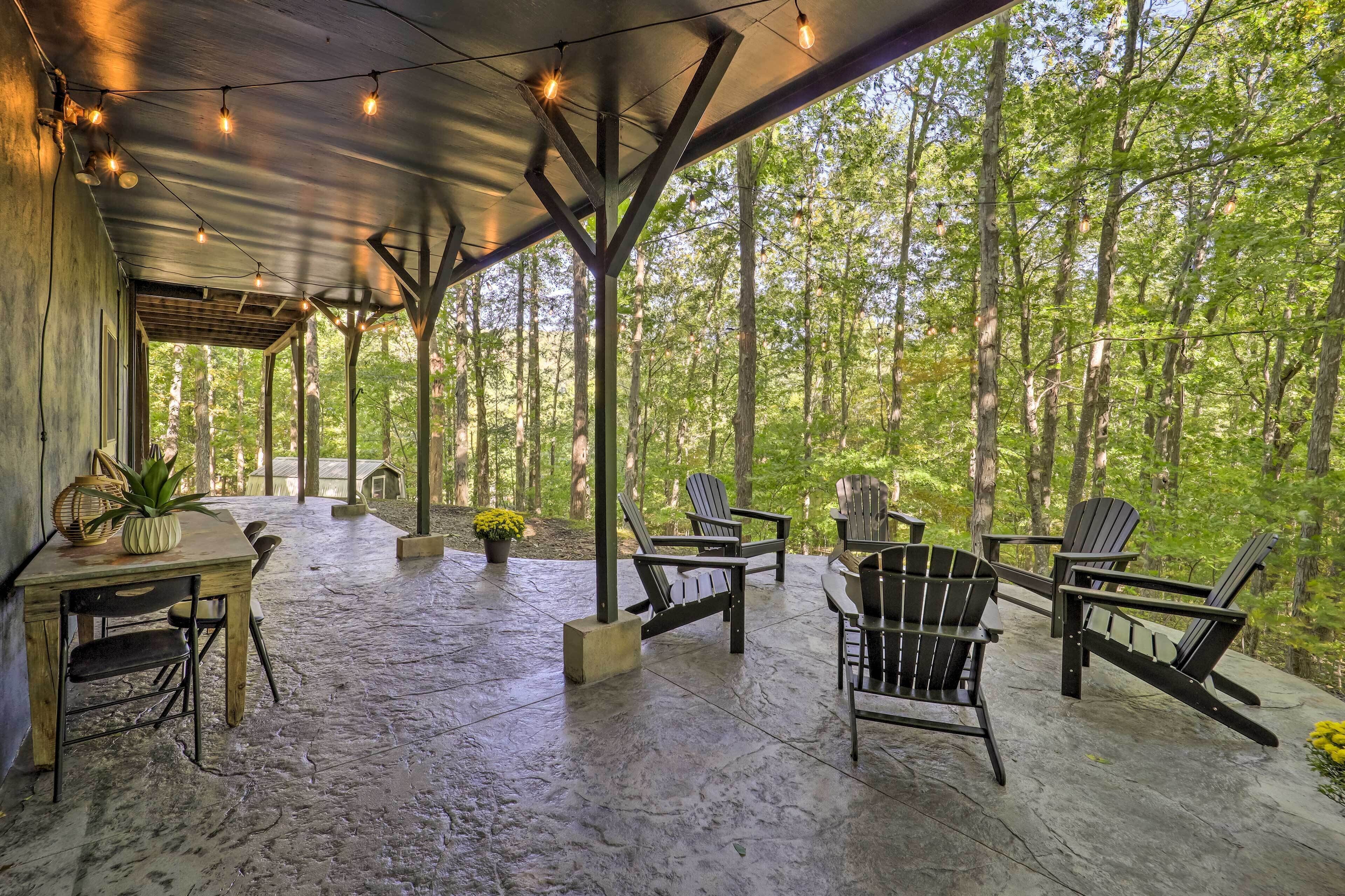 A covered outdoor seating area with Adirondack chairs, a table, and string lights.