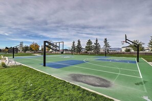 Un terrain de basket avec des marquages verts et bleus, entouré d’herbe et d’arbres.