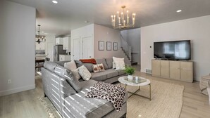 A modern living room with a grey sofa, a coffee table, and a TV on a cabinet. - Lovely Vineyard Getaway < 1 Mi to Utah Lake! (Orem)