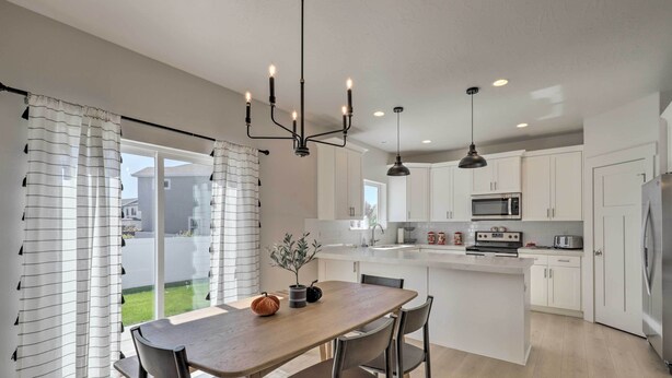 A modern kitchen with white cabinets, a central island, and a dining area with a wooden table and chairs. - Lovely Vineyard Getaway < 1 Mi to Utah Lake! (Orem)