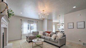 A spacious living room with a grey sofa, a round coffee table, and a chandelier. - Lovely Vineyard Getaway < 1 Mi to Utah Lake! (Orem)