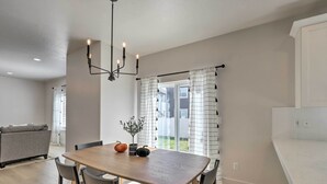 A modern kitchen with a wooden table and chairs, a hanging light fixture, and a view of the backyard through a sliding glass door. - Lovely Vineyard Getaway < 1 Mi to Utah Lake! (Orem)