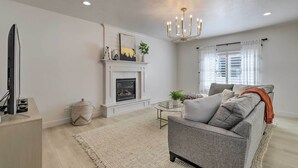 A living room with a fireplace, a sofa, a television, and a chandelier. - Lovely Vineyard Getaway < 1 Mi to Utah Lake! (Orem)