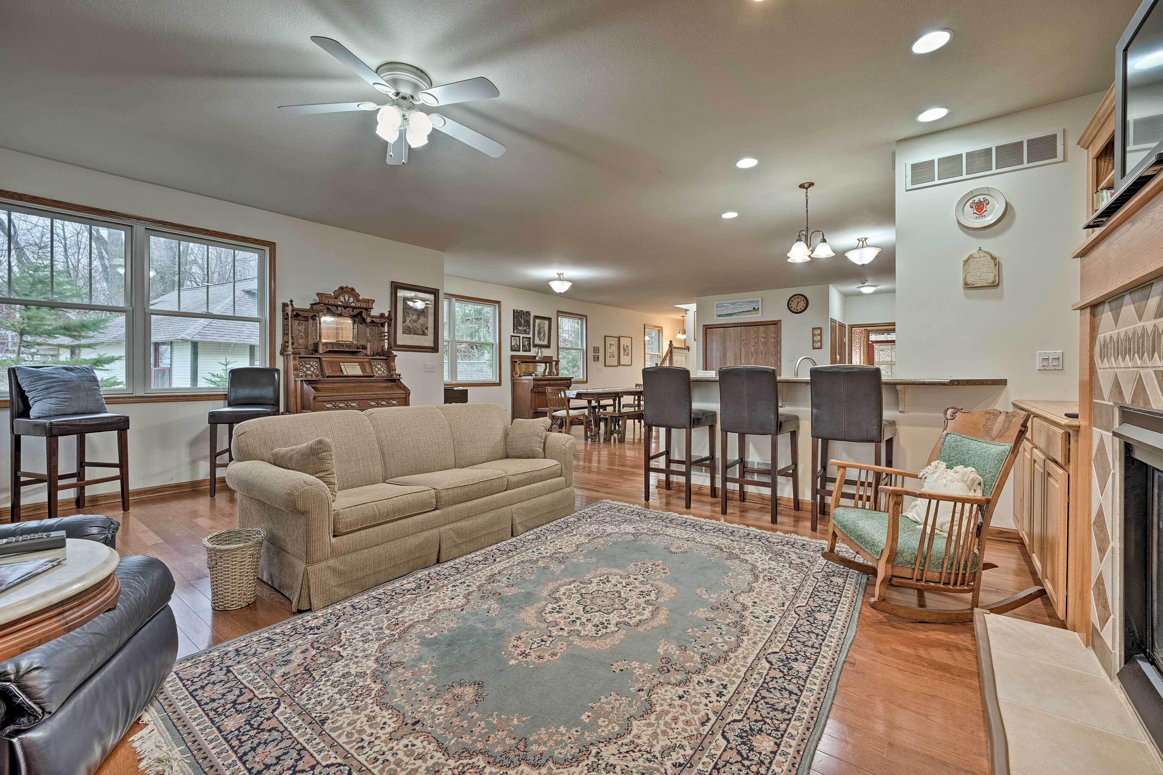 A spacious living room with a large sofa, a wooden rocking chair, a fireplace, and a dining area with a wooden table and chairs.