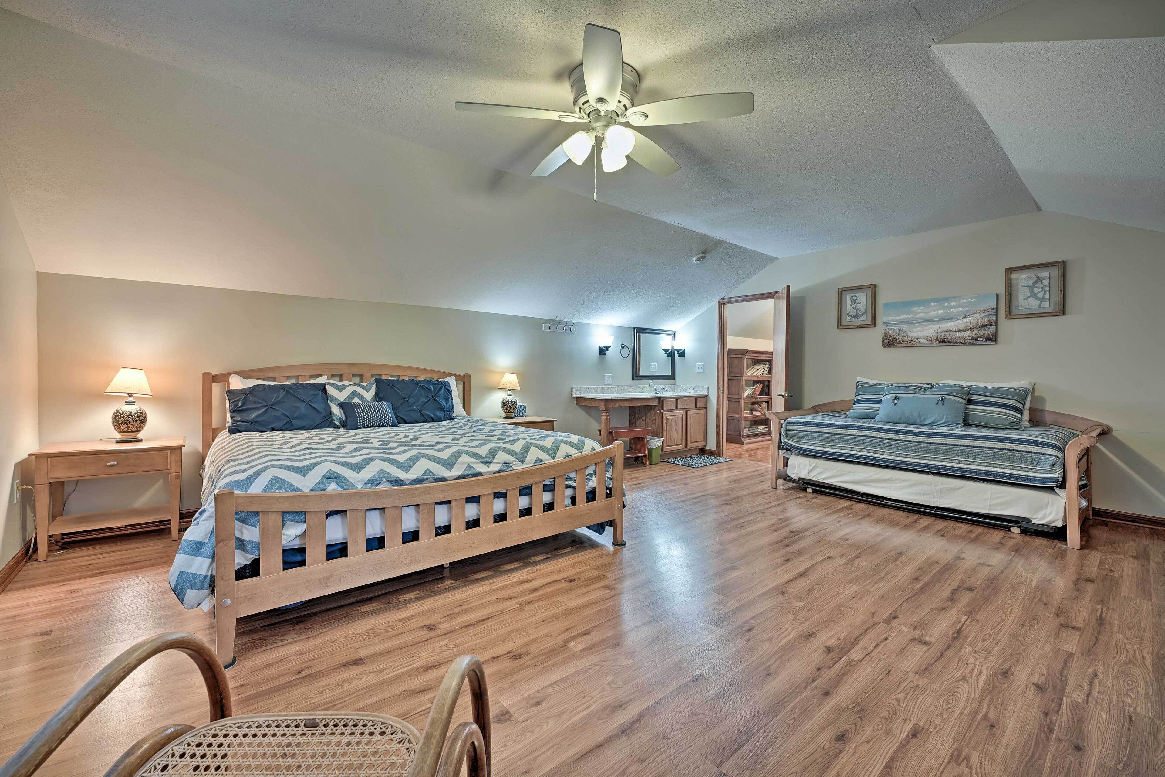 A bedroom with a wooden bed, a desk, a chair, a ceiling fan, and a large window.