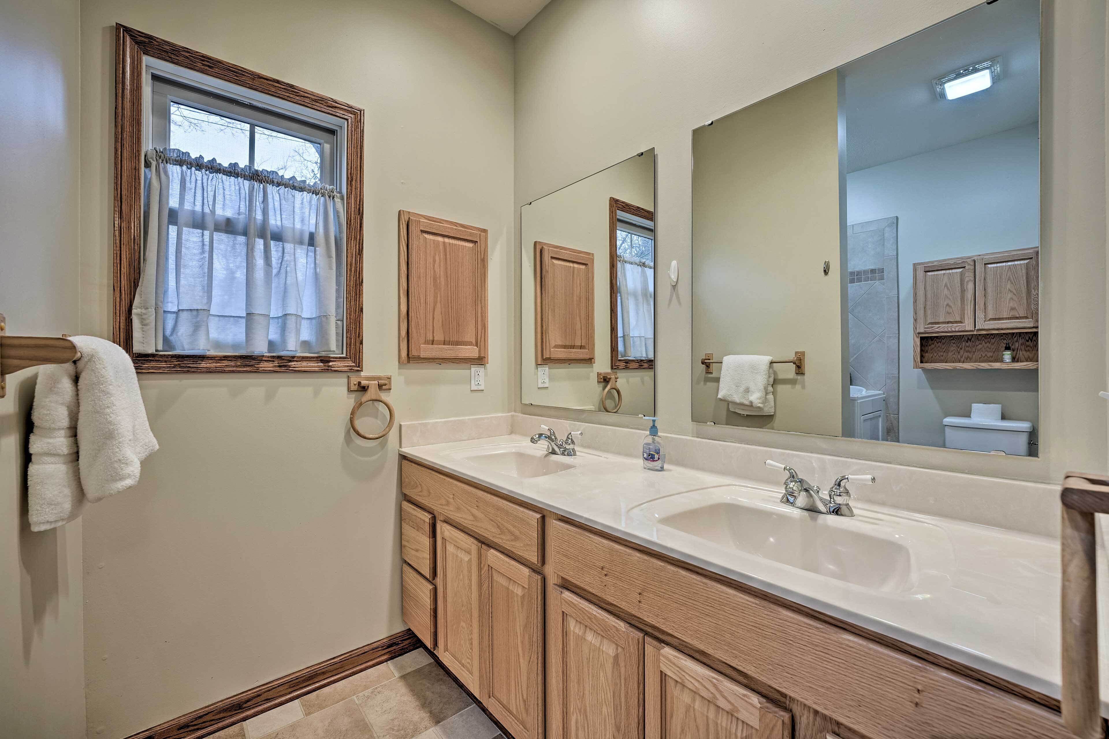 Une salle de bain avec deux lavabos, des meubles en bois, un grand miroir et une fenêtre avec des rideaux.