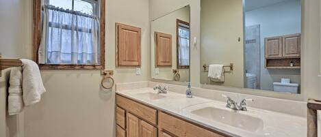 Une salle de bain avec deux lavabos, des meubles en bois, un grand miroir et une fenêtre avec des rideaux.