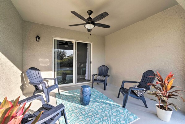 A covered patio with a ceiling fan, two chairs, a table, and a potted plant.