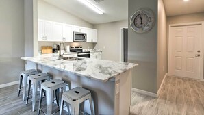 Una cocina moderna con armarios blancos, una isla de mármol y taburetes de bar.