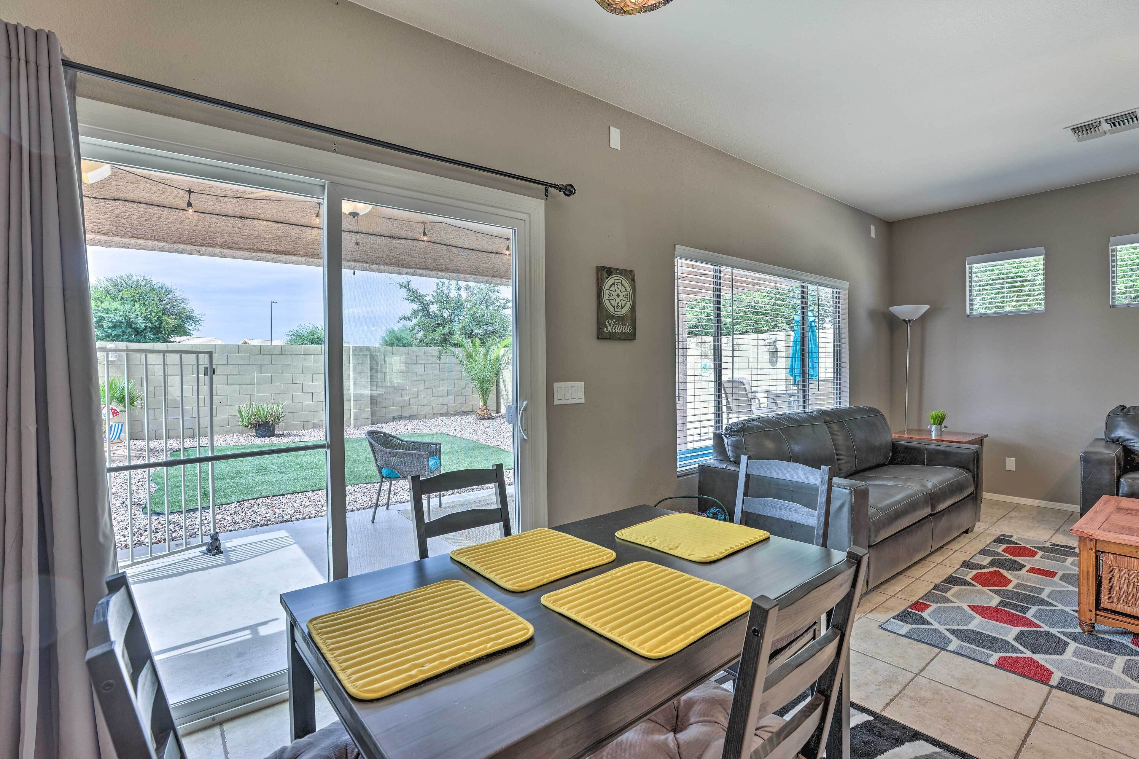 A spacious living area with a sliding glass door leading to a patio, a dark leather sofa, a dining table with yellow placemats, and a patterned rug.