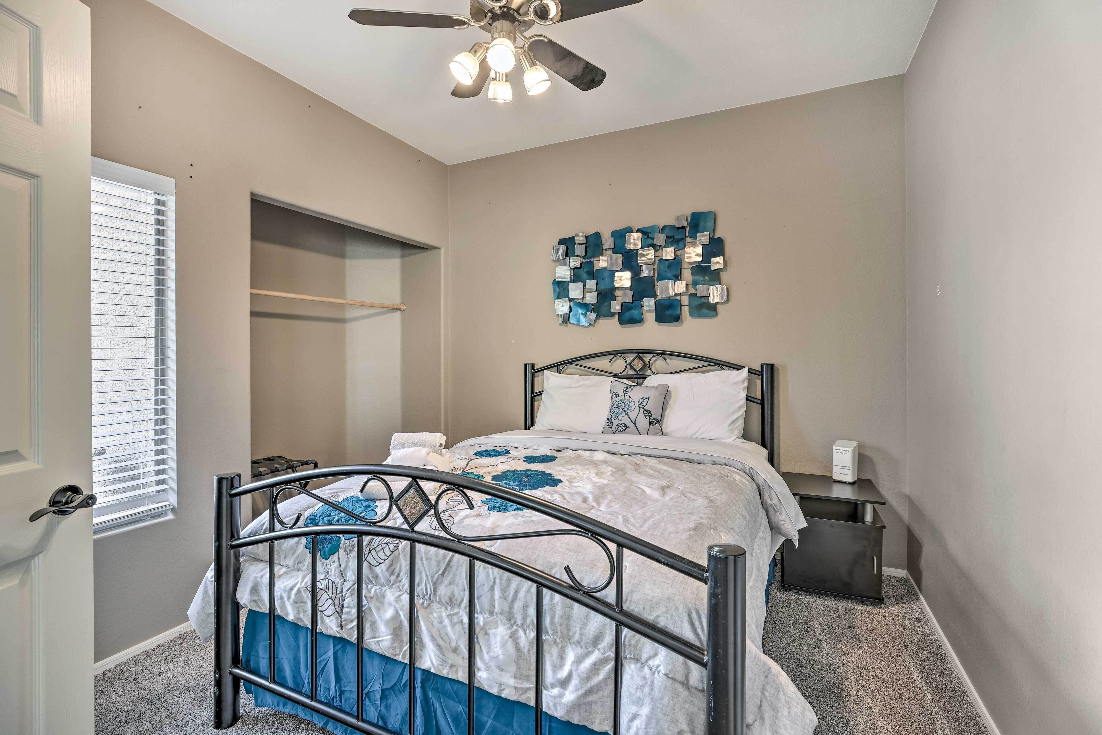 A bedroom with a bed, a ceiling fan, a wall art piece, and a window with blinds.