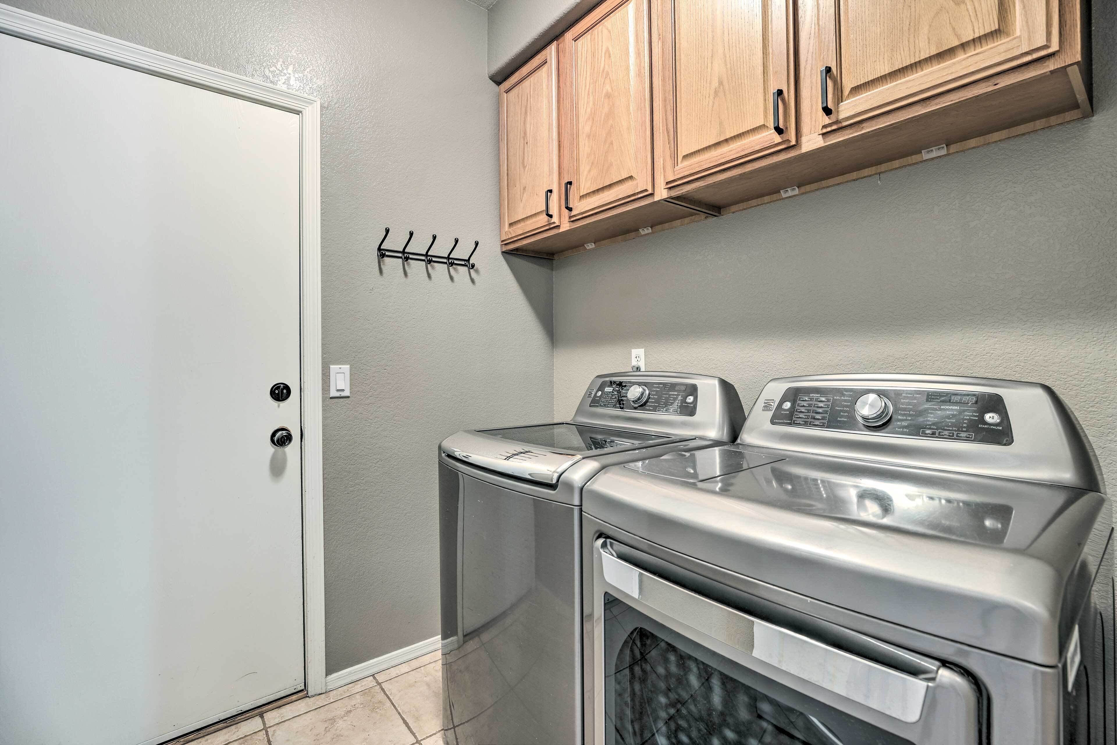 A laundry room with a front-loading washer and dryer, wooden cabinets above, and a door with a coat rack.