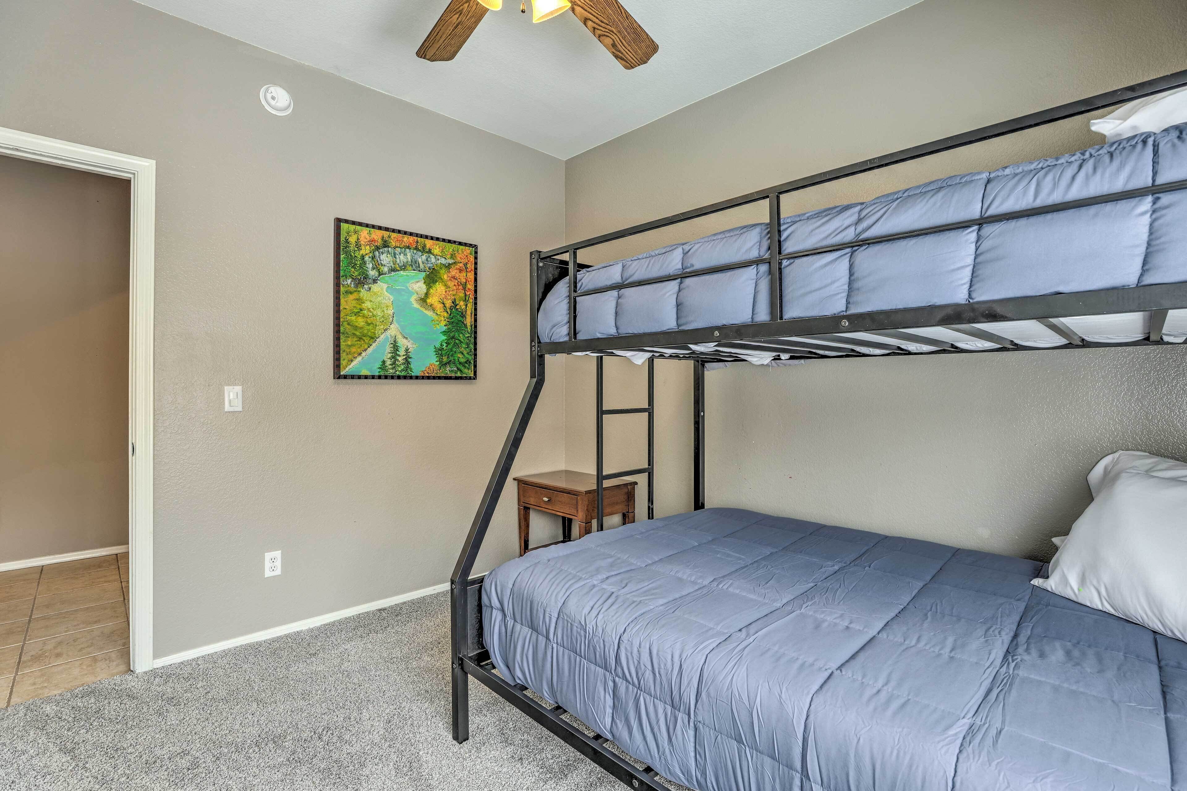 A bunk bed with a blue mattress, a small wooden nightstand, and a painting of a landscape on the wall.