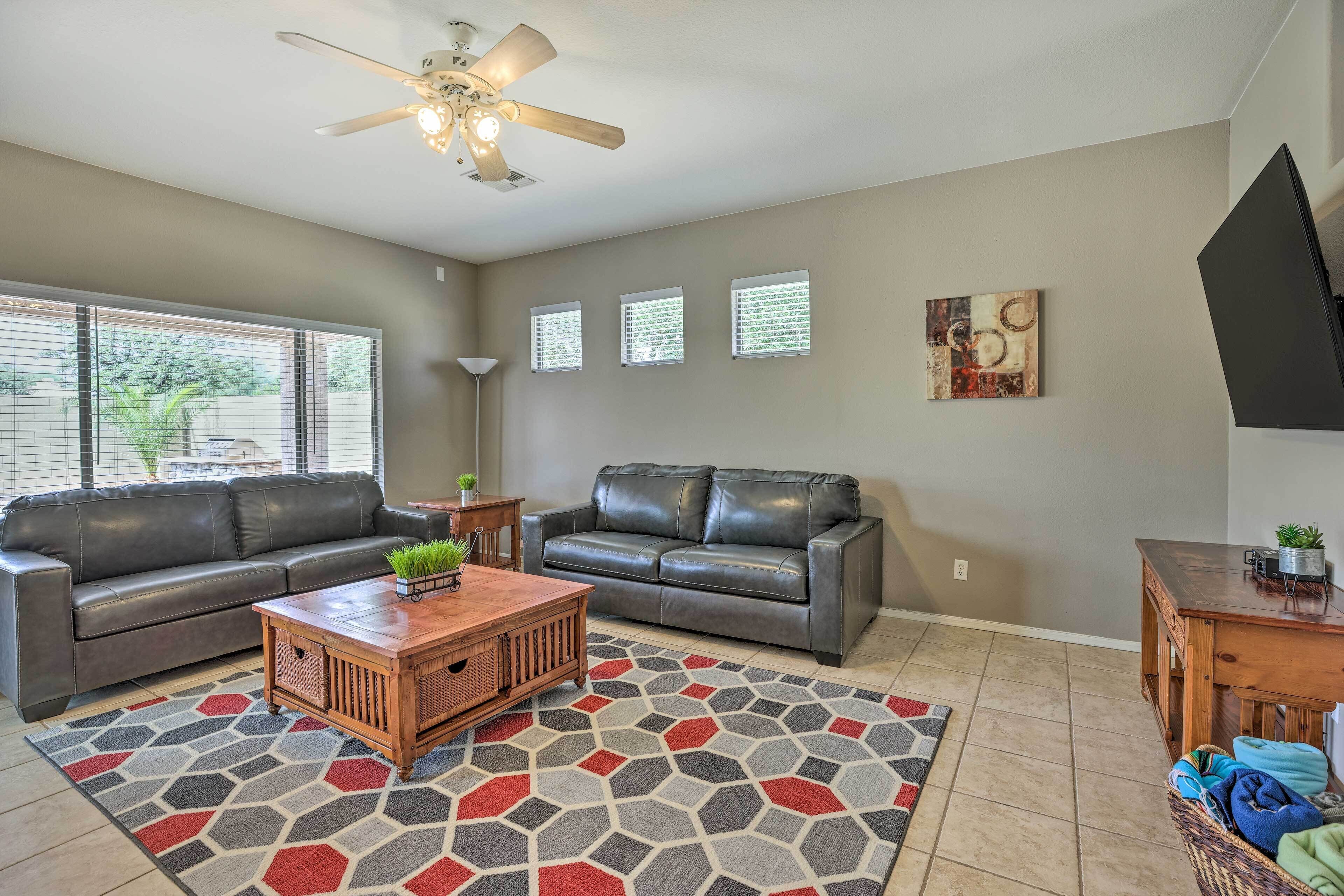 A living room with two leather sofas, a wooden coffee table, a patterned rug, a ceiling fan, and a TV stand with a plant.