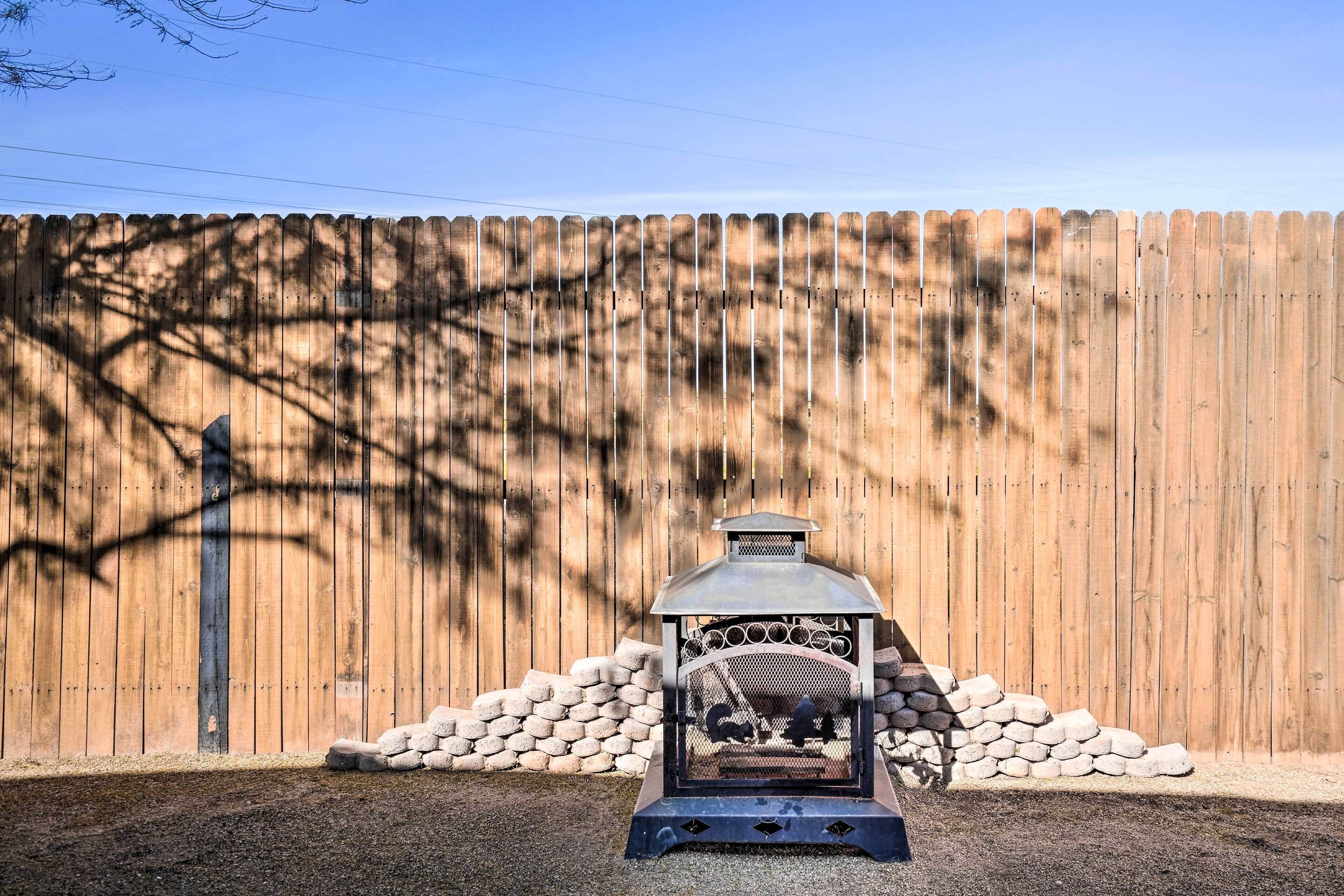 A metal barbecue grill with a chimney, surrounded by a wooden fence and stone walls.