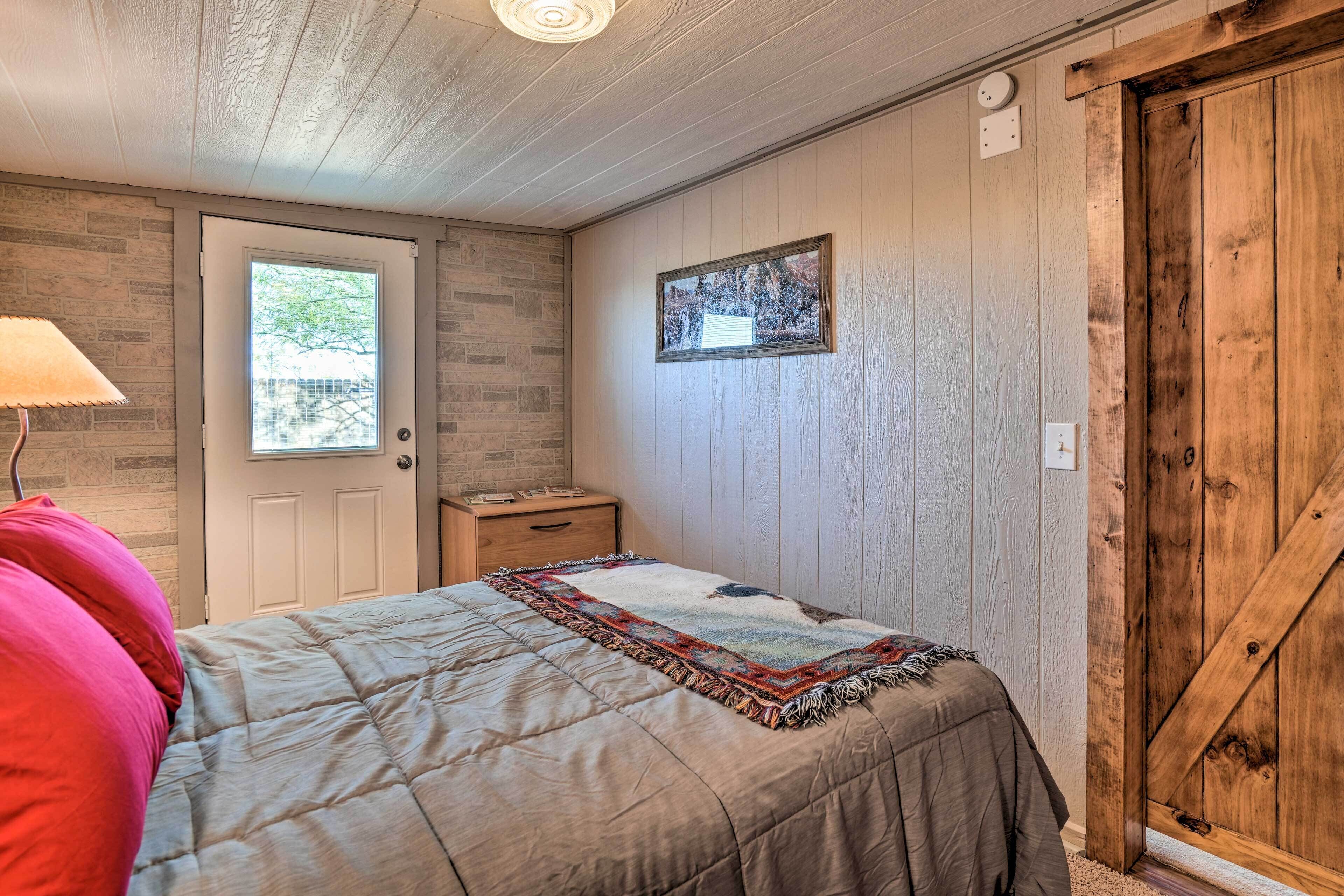 Une chambre à coucher comprenant un lit, une table de chevet, une lampe, une porte, une fenêtre et un panneau mural en bois.