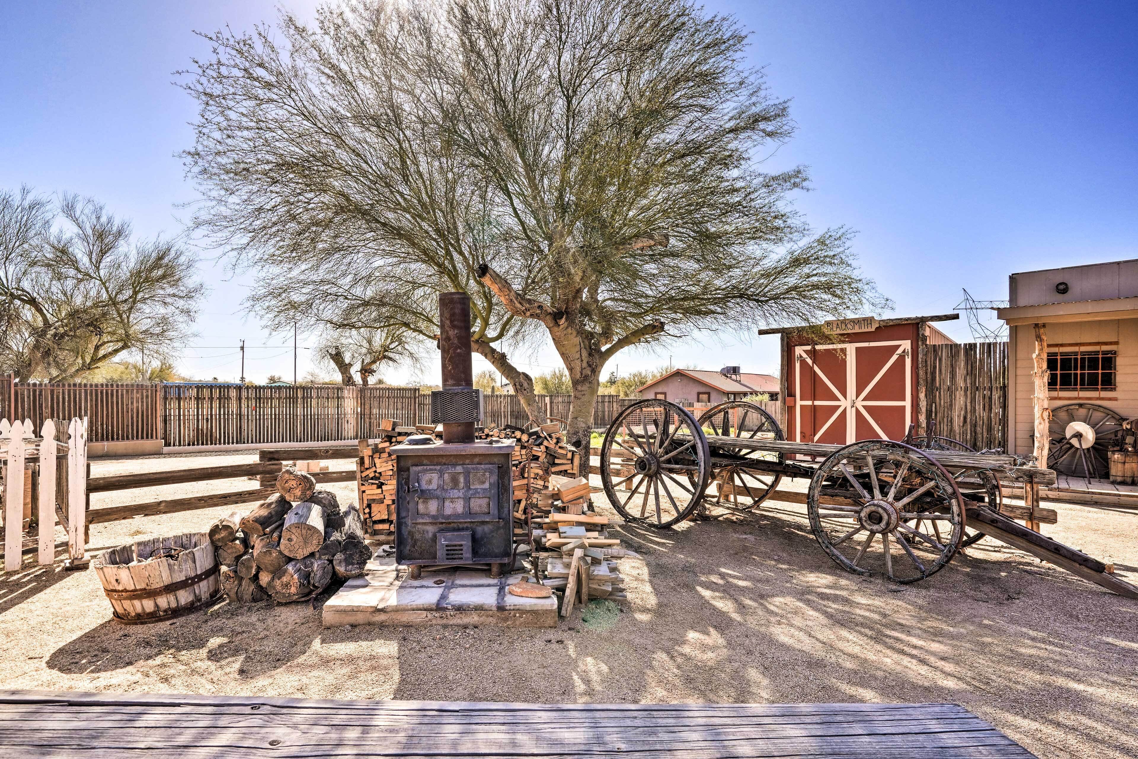 A rustic outdoor setting with a wood-burning stove, a wooden cart, and a large tree.