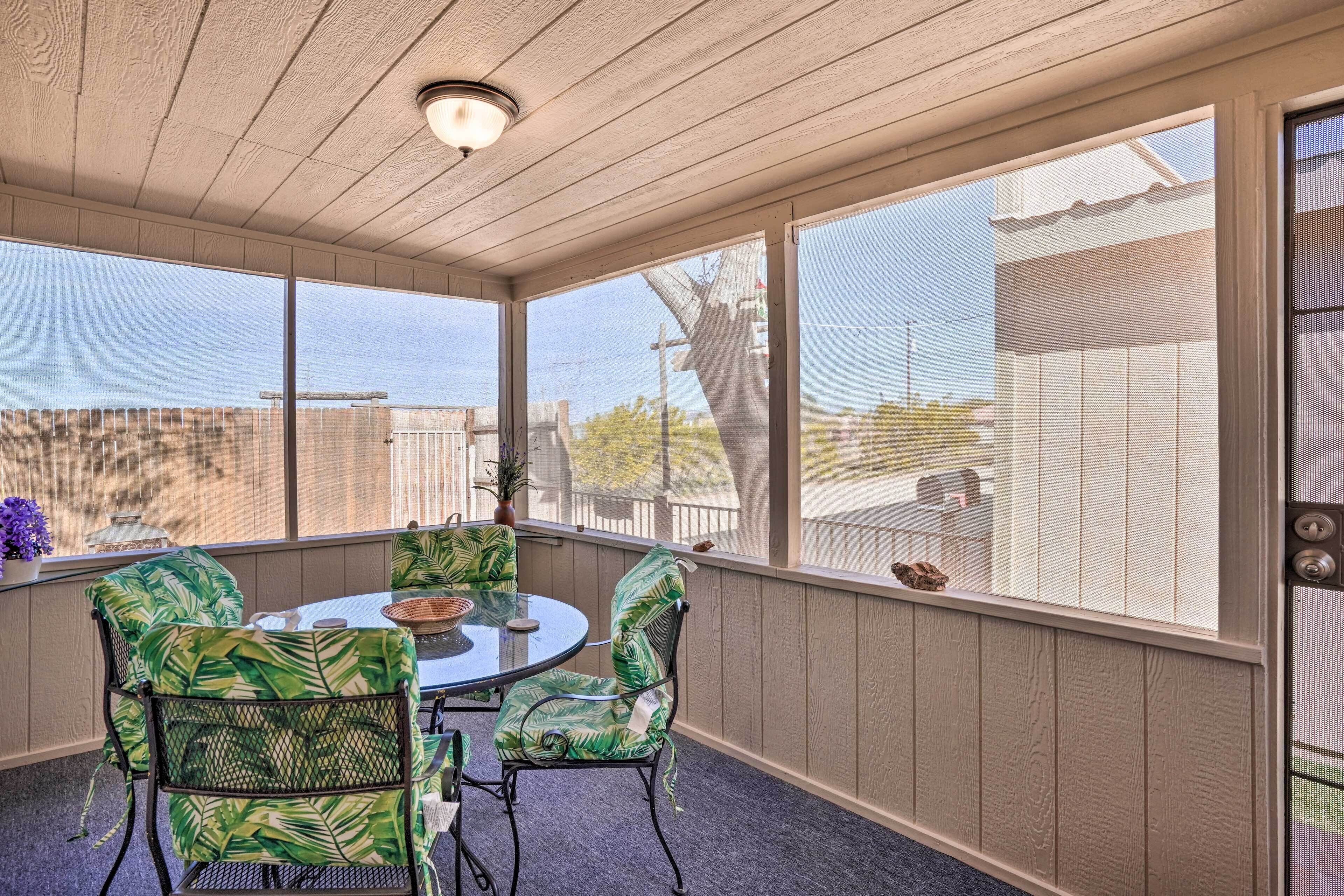 A covered patio with a round table and chairs, large windows, and a view of the outside.