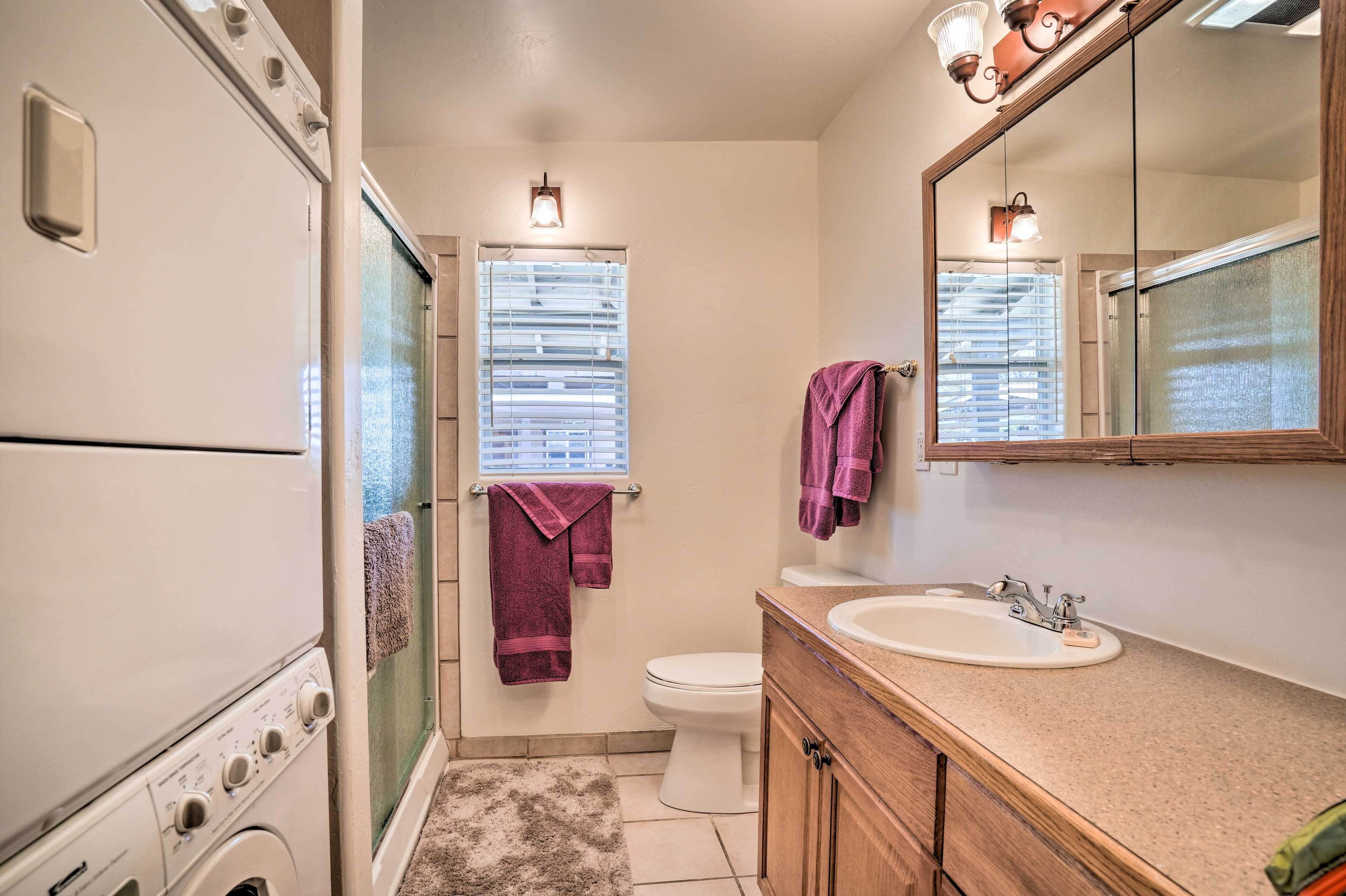 A compact bathroom with a washing machine, a toilet, a sink, and a mirror.