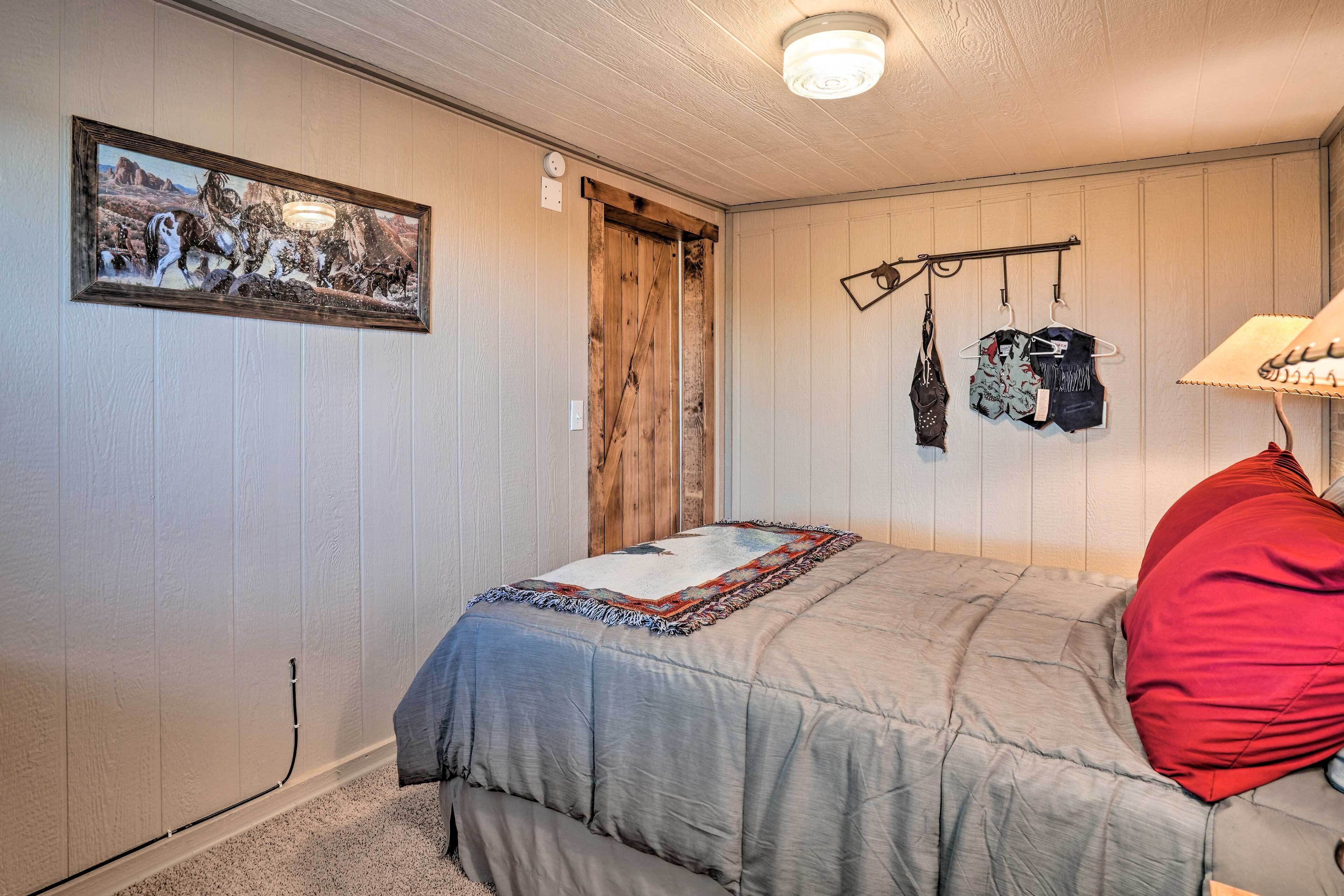 Un dormitorio con cama, una puerta, un perchero y un cuadro en la pared.