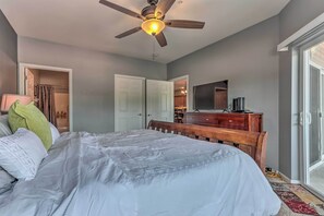 A bedroom with a bed, ceiling fan, and a view of the kitchen and living area through an open door. - Lake & Poolside Fun! Water-view Camdenton Condo (Camdenton)