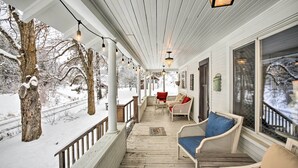 A covered porch with white wooden railings, a wooden table, and two wicker chairs with cushions. - Modern Farmhouse w/ Movie Room - 6 Mi to Lake! (Coeur d'Alene)