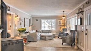 A cozy living room with a fireplace, a sofa, a patterned armchair, and a dining table. - Modern Farmhouse w/ Movie Room - 6 Mi to Lake! (Coeur d'Alene)