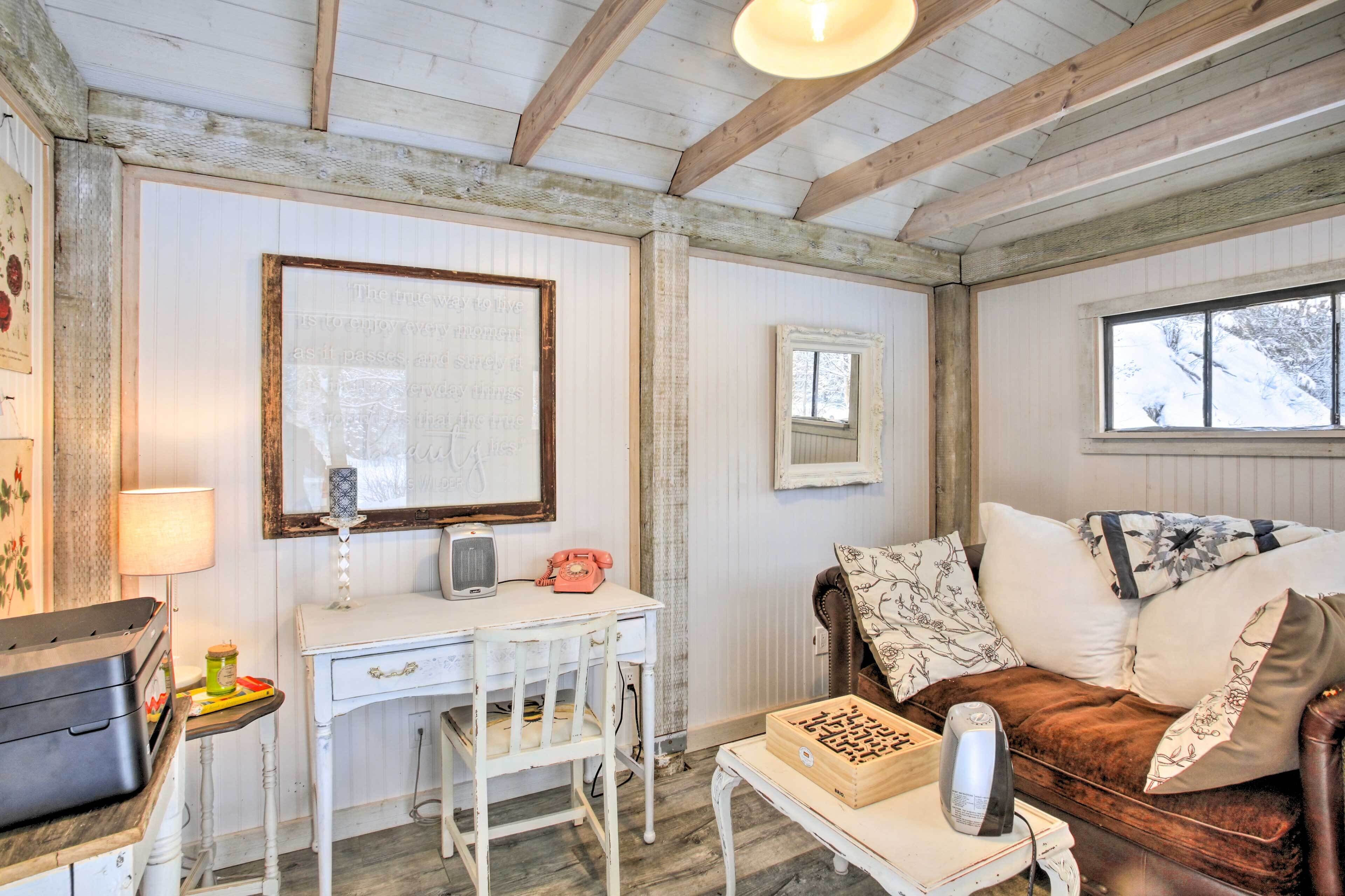 A rustic room with a white desk, a vintage telephone, a wooden chest, and a brown leather couch with floral cushions.