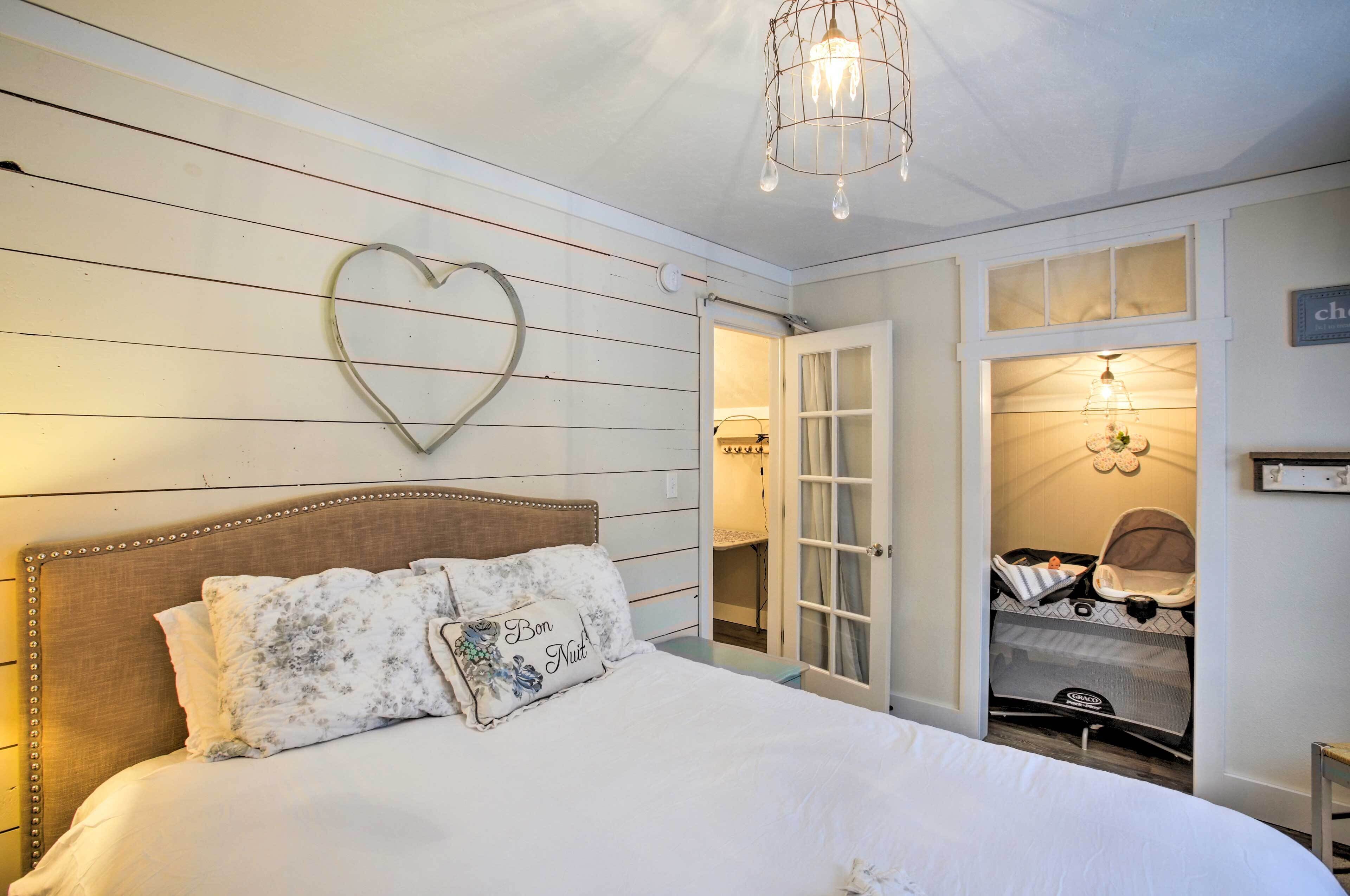 Une chambre à coucher avec un lit, un décor en forme de cœur sur le mur, un lustre et un berceau dans la pièce adjacente.