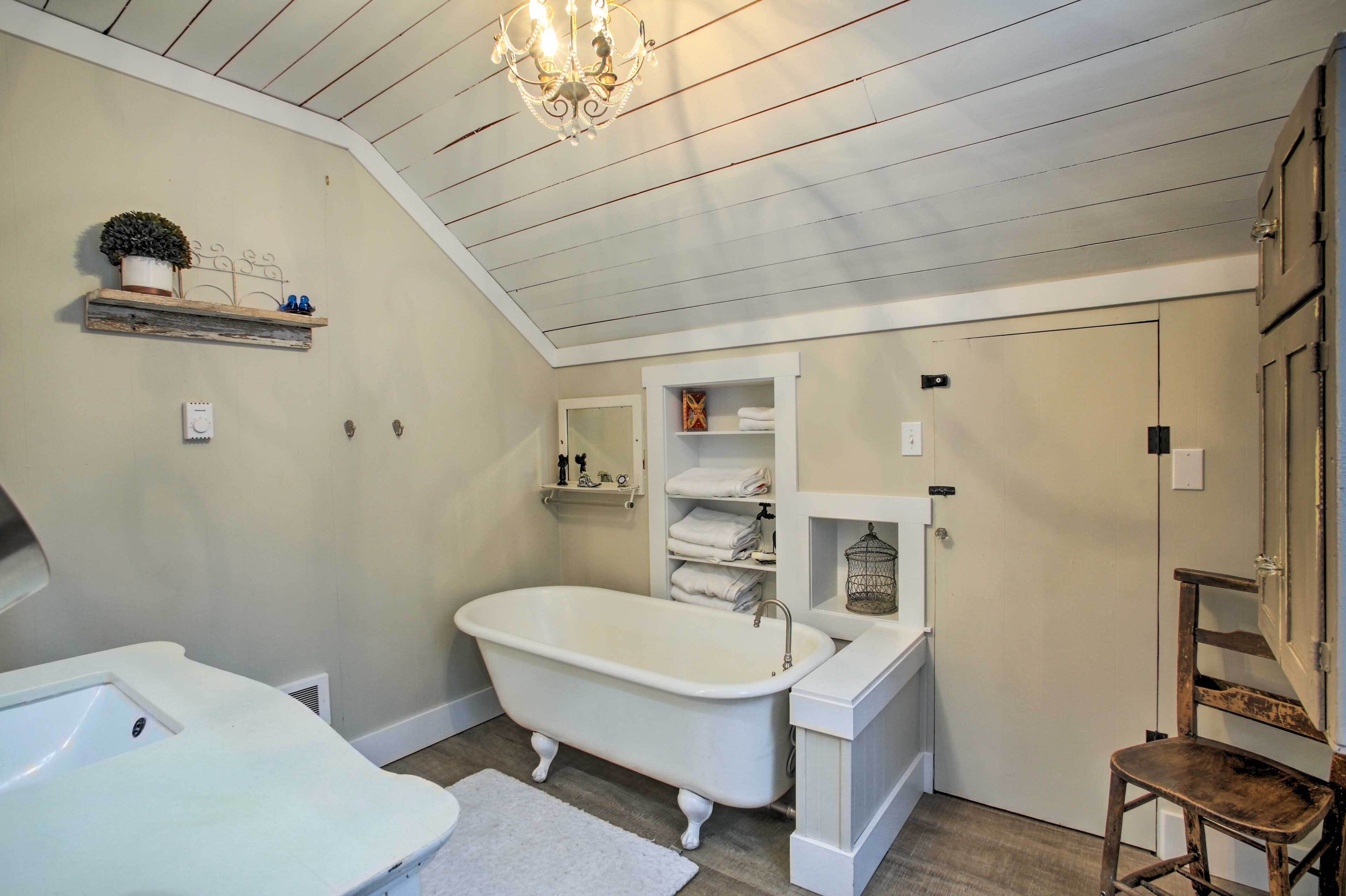 A bathroom with a freestanding bathtub, a vanity with a mirror, and a wooden chair.
