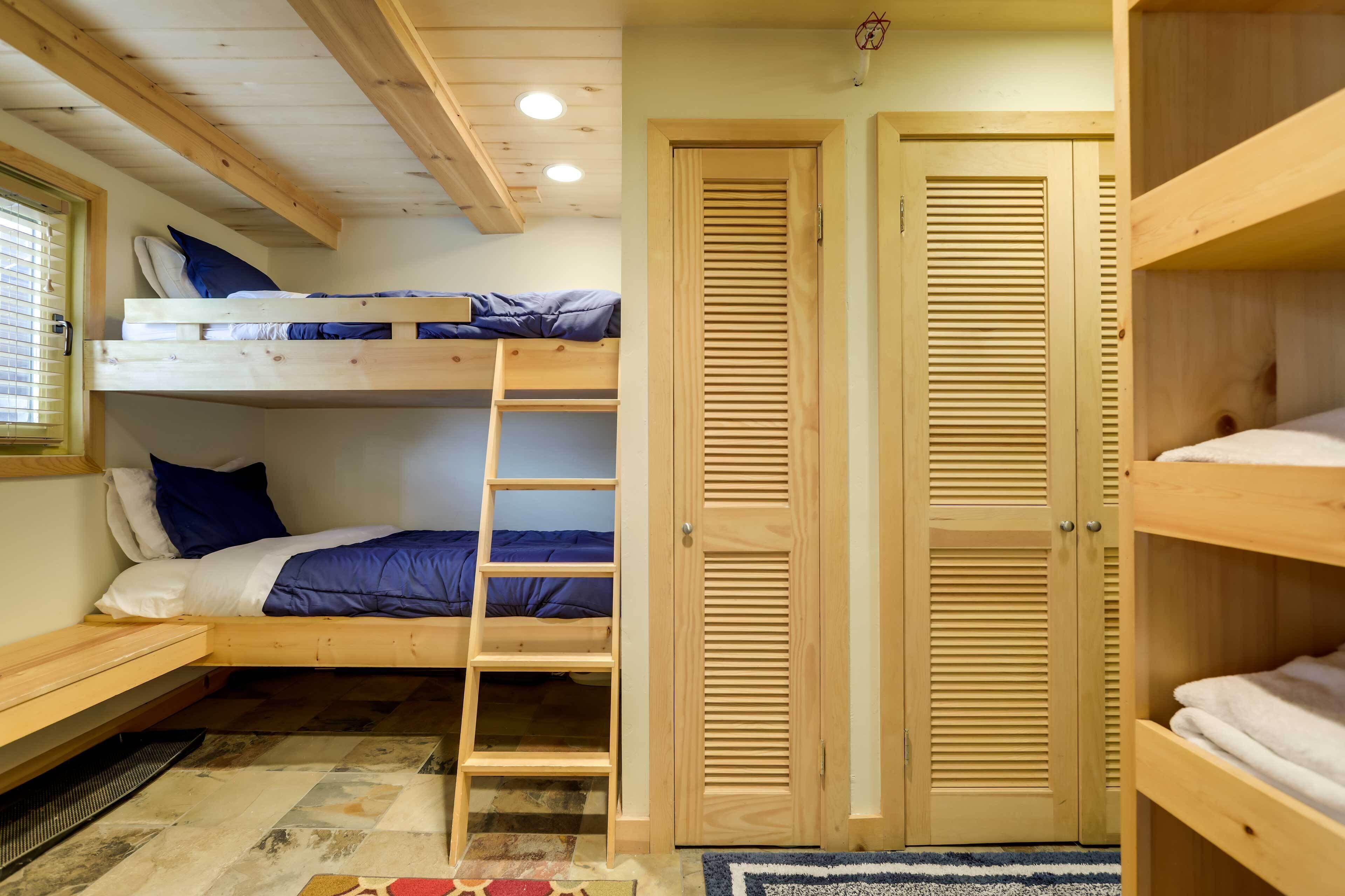 A bunk bed room with a wooden ladder, two wooden doors, and a window with blinds.