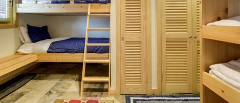 A bunk bed room with a wooden ladder, two wooden doors, and a window with blinds.