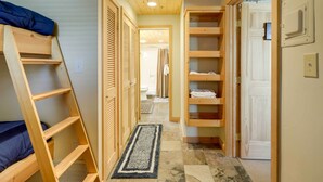 Un pasillo estrecho con una escalera de madera, estanterías de madera y una puerta que da a un baño.