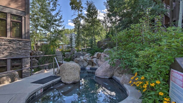 Una piscina de hidromasaje rodeada de rocas y vegetación, con un cartel de advertencia para usuarios de la piscina.