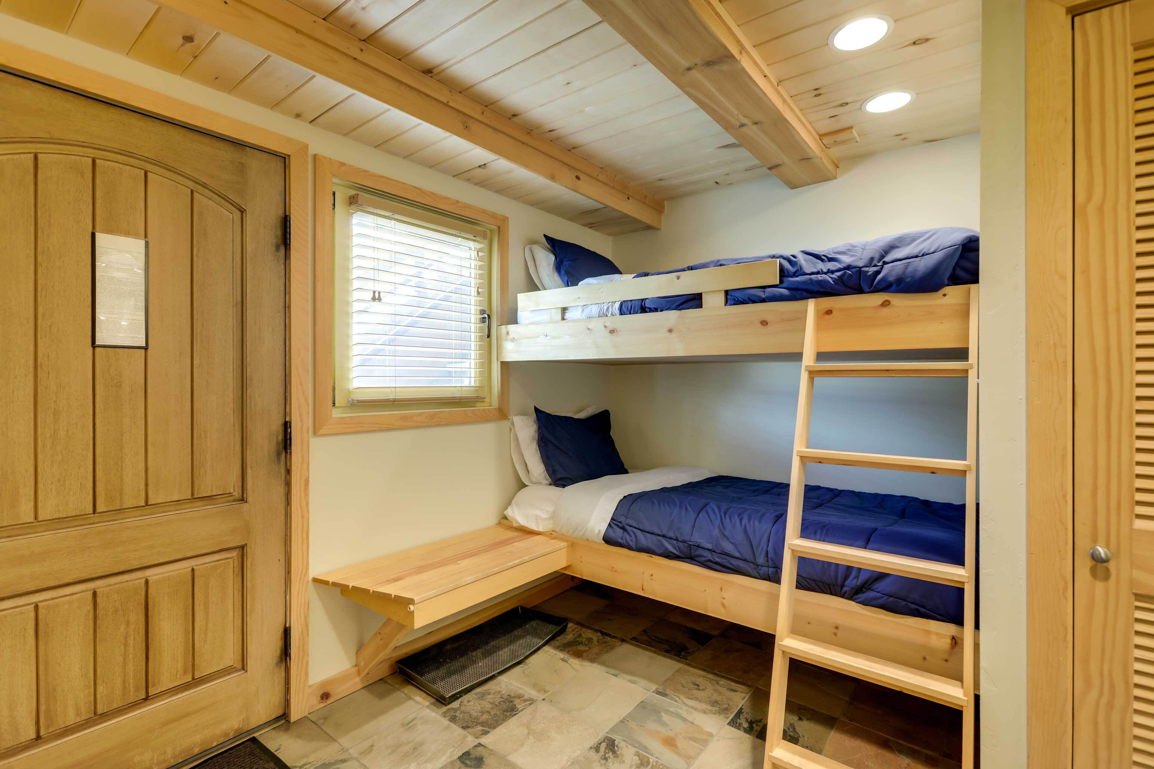 A bunk bed room with a wooden door, a window with blinds, and a small desk.