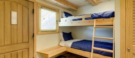 A bunk bed room with a wooden door, a window with blinds, and a small desk.
