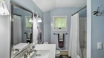 A bathroom with a white sink, mirror, and toilet, a window with blinds, and a shower curtain.