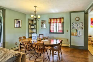 A dining area with a wooden table and chairs, a chandelier, and a window with curtains. - Finger Lakes Home w/ Sweeping Views and Sun Deck! (Watkins Glen)