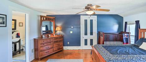 A bedroom with a bed, dresser, mirror, ceiling fan, and a door leading to another room.