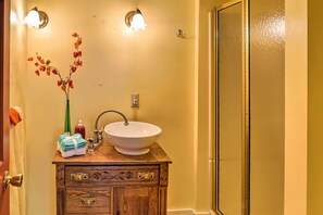 A bathroom with a wooden vanity, a white sink, and a mirror. There is a vase with flowers on the vanity and a towel rack above the sink. - Finger Lakes Home w/ Sweeping Views and Sun Deck! (Watkins Glen)