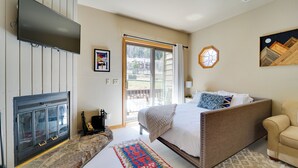 A bedroom with a fireplace, a large bed, a sofa, a TV, and a view of the outdoors.