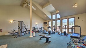 A spacious gym with various exercise equipment, large windows, and a ceiling fan.