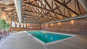 An indoor swimming pool with a wooden ceiling and walls, surrounded by seating areas.